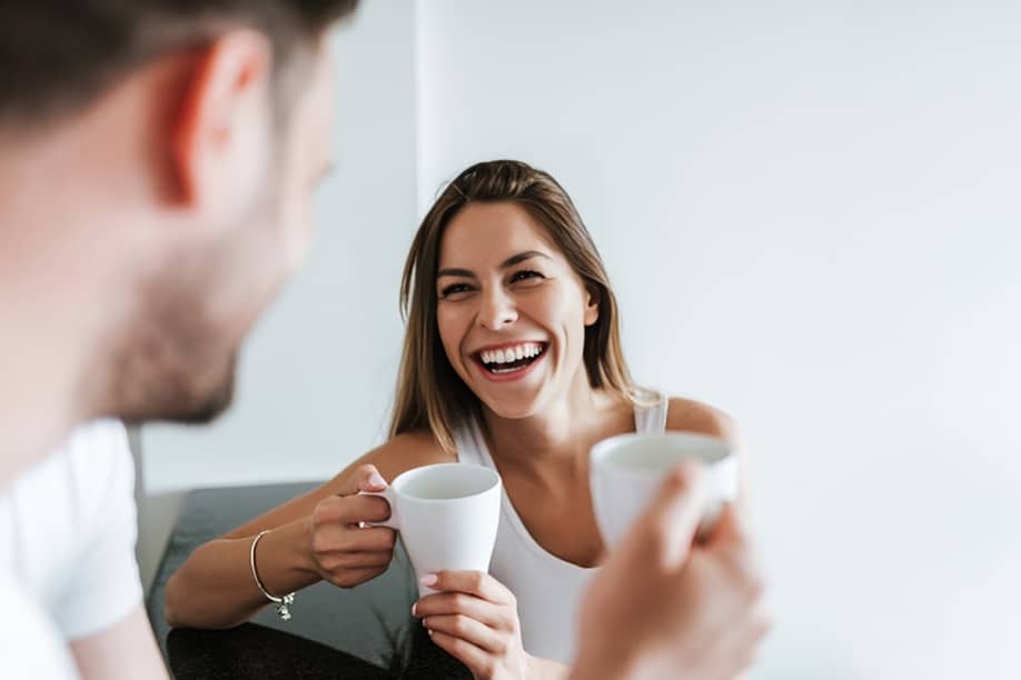Two people smiling while holding coffee cups in a bright, modern dental office setting.