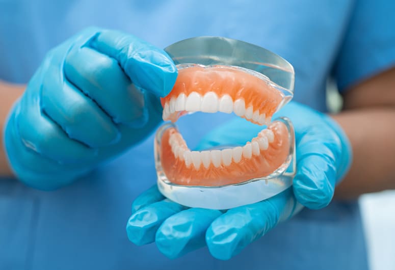 Dentist in blue gloves holding dental model showing teeth arrangement for educational demonstration.
