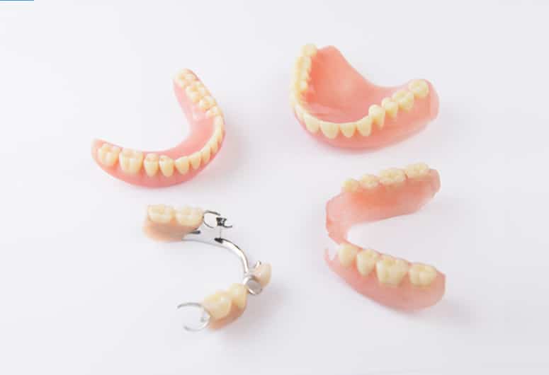 Denture models and components displayed on white surface showing various dental prosthetics and parts.