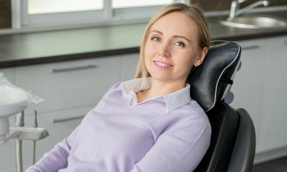 Professional woman in purple shirt smiling while seated in dental office chair.