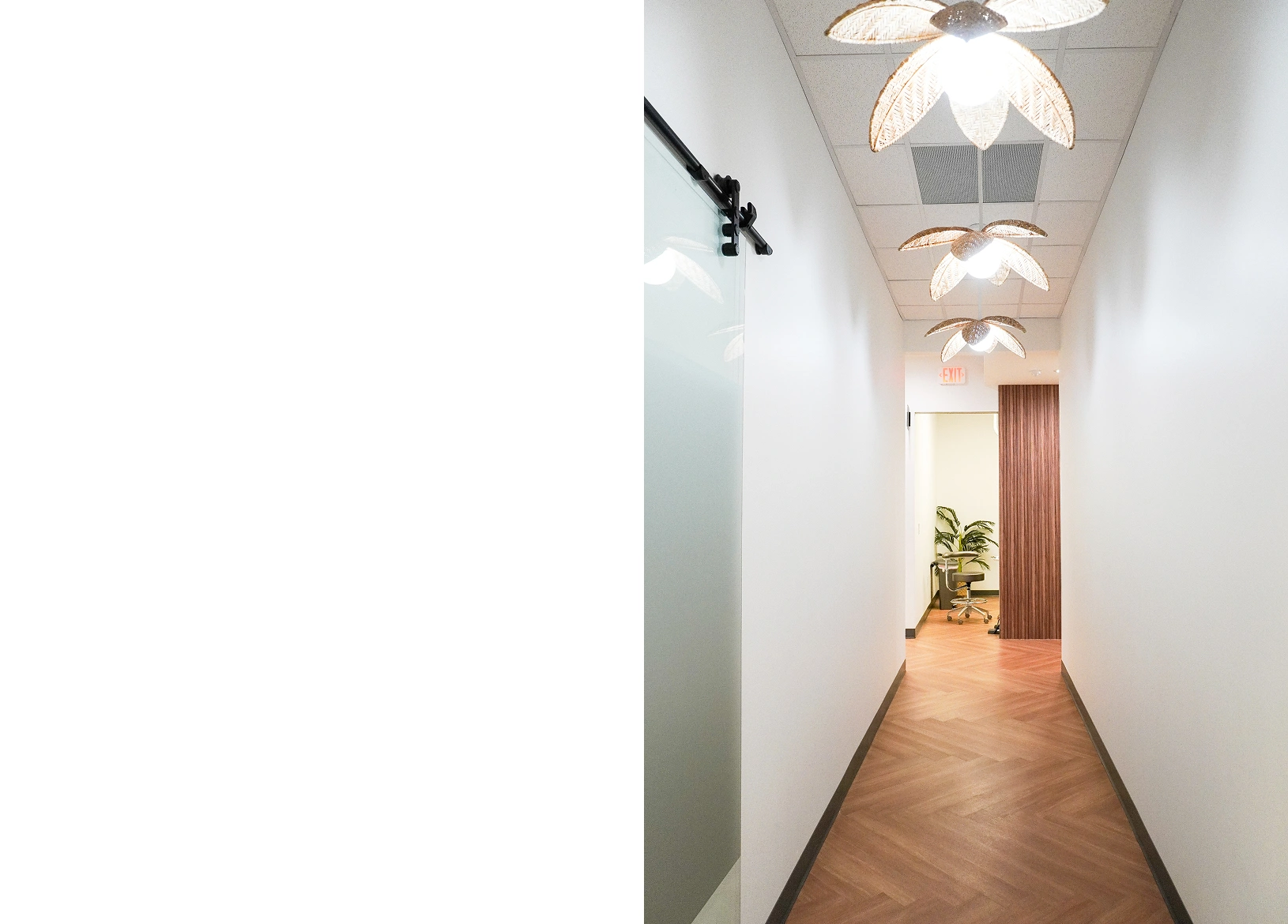 Clean, modern dental office hallway with white walls, wooden flooring, and skylights overhead.