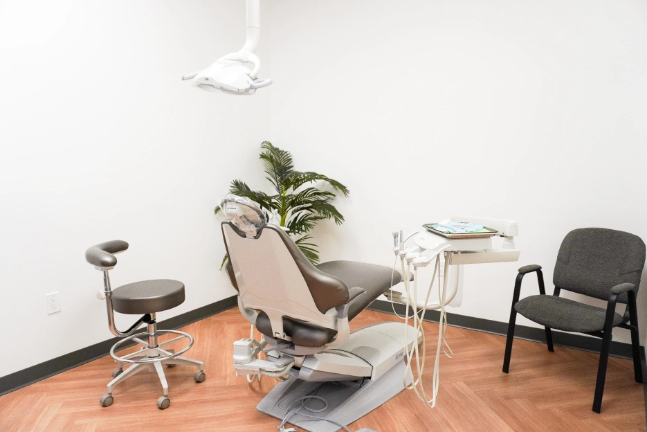 Dental examination room with chair, overhead light, potted plant, and waiting seating area.
