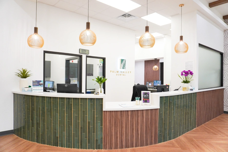 Modern dental office reception area with curved green and red wood desk, pendant lights, and plants.