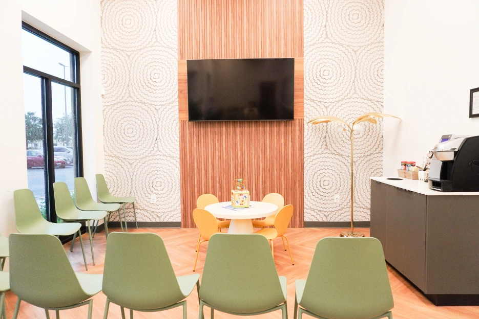 Modern dental office waiting room with green chairs, TV, and reception desk