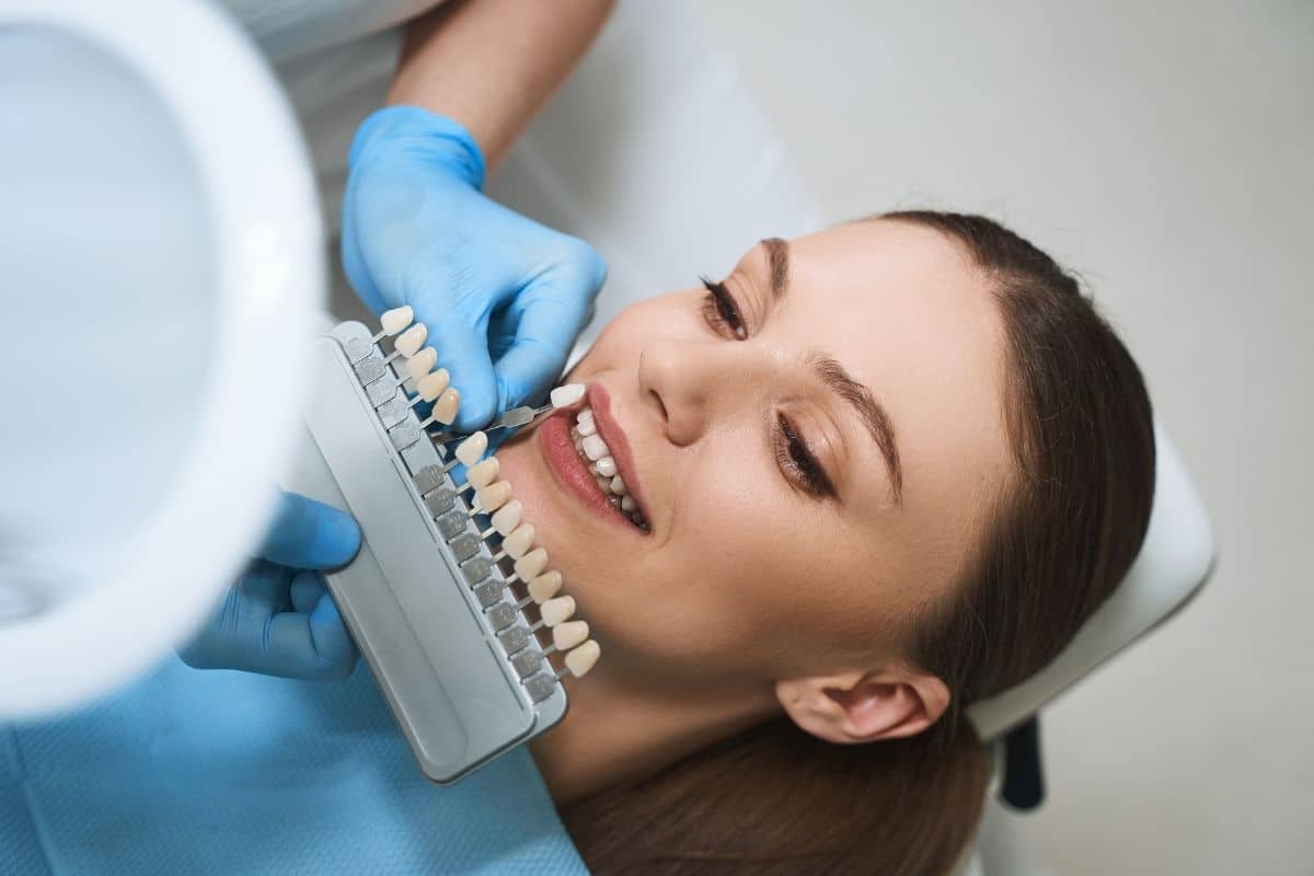 Dentist comparing tooth shade samples to patient's smile during veneer consultation.