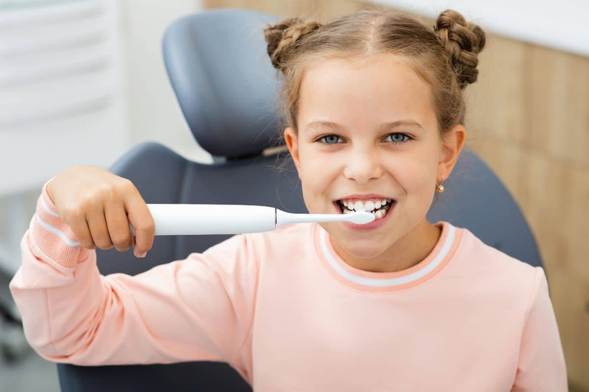 Smiling child brushing teeth in dental chair during pediatric checkup.