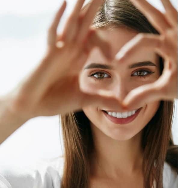 Happy patient making a heart shape with hands framing her bright smile.