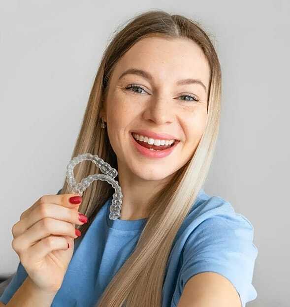 Happy woman holding clear Invisalign aligners for orthodontic treatment in Edinburg.